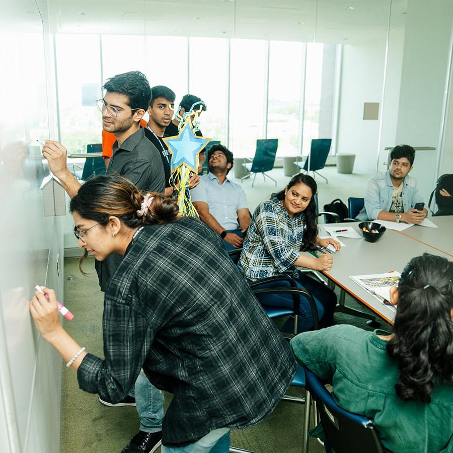 Graduate students write on whiteboard in seminar room.